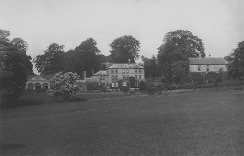 Black and white photo showing Ford House, a relatively simple Georgian house, positioned on a slope, surrounded by trees.